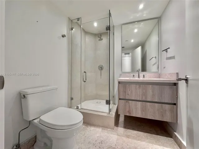 Glass-enclosed shower with a tiled interior, floating vanity with wood-finish cabinetry, and a framed mirror