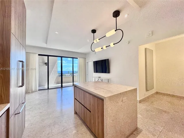 Open-concept living area with large format tile flooring, a kitchen island with a stone finish countertop, built-in wood-finish cabinetry, and a modern linear chandelier