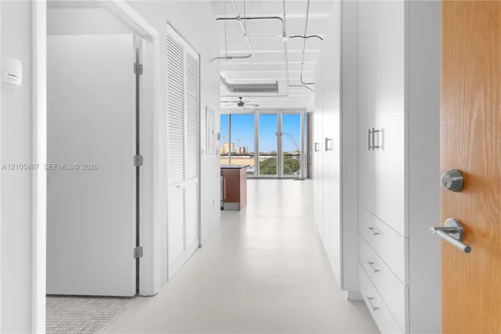 Light wood-finish entry door, smooth flooring, white built-in storage cabinetry, louvered closet doors, and exposed ceiling ductwork