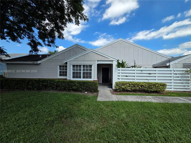 Single-story exterior featuring light-toned horizontal siding, multi-gabled rooflines, decorative gable accents, a concrete walkway, and a private white slatted fence