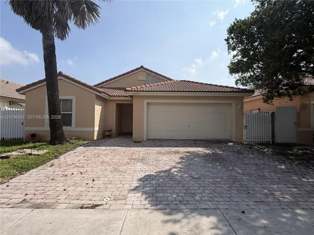 Stucco exterior with a tiled roof, paver driveway, and an attached two-car garage