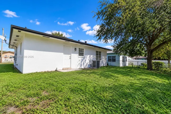 Expansive backyard featuring a mature tree, stucco exterior, black roofline, and visible HVAC unit