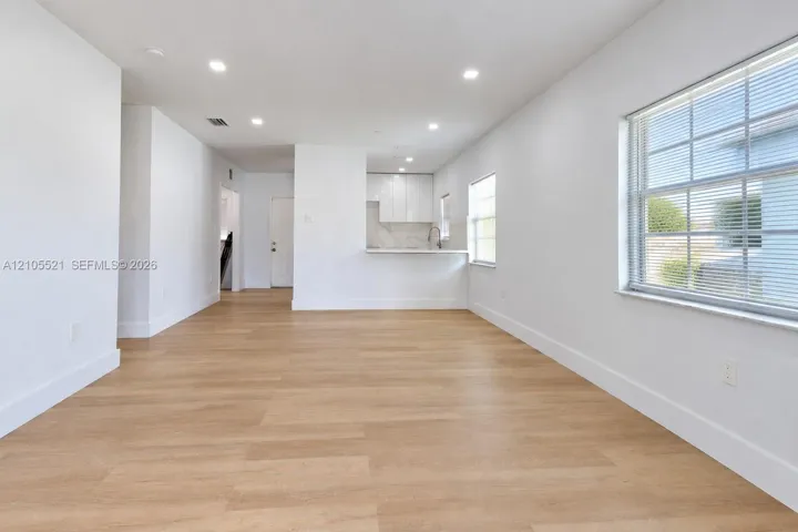 Open-concept living area featuring wood-finish flooring, recessed lighting, white walls, and a kitchen pass-through with a breakfast bar