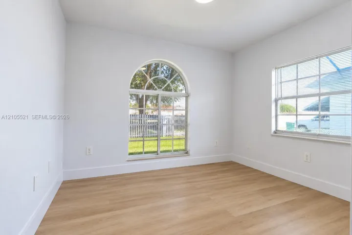 Arch-top window, wood-finish flooring, white baseboards, recessed lighting, white walls