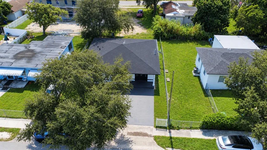 Paved driveway entrance with a dark shingle roof, mature tree, and a grass lawn
