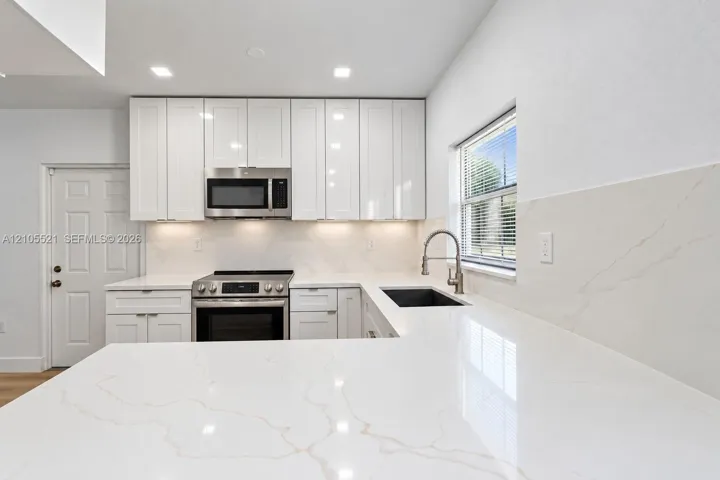 White shaker-style cabinetry with under-cabinet lighting, stainless steel appliances, and a stainless steel sink with a gooseneck faucet