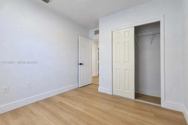 Light wood-finish flooring with white baseboards, a white paneled door with a black handle, and a white sliding closet door