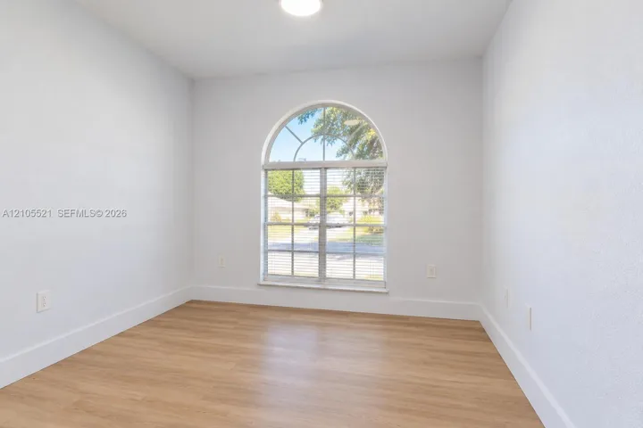 Arched window with blinds, wood-finish flooring, white walls, and a ceiling light fixture