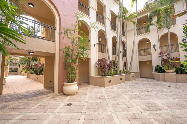 Courtyard entry with paver flooring, arched walkways, decorative iron railings, and integrated planter beds