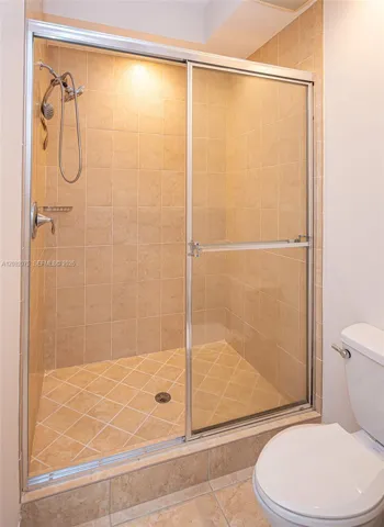Tiled shower with sliding glass enclosure, integrated shower head, and an overhead light fixture