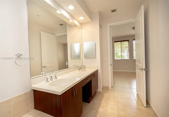 Dual vanity with integrated sinks, expansive mirror, wood-finish cabinetry, and tiled flooring
