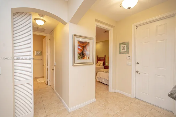 Foyer featuring tiled flooring, a white paneled entry door, arched doorway, and built-in overhead lighting
