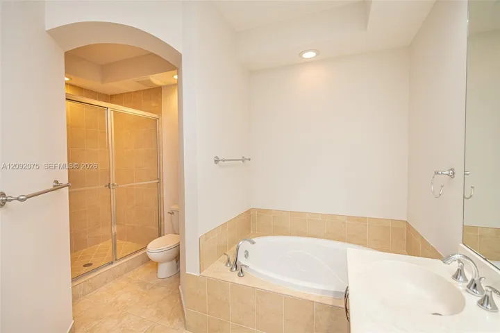 Recessed lighting, arched doorway, tile flooring, built-in bathtub, and a glass-enclosed shower