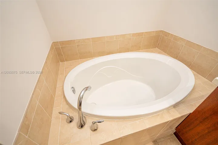 Oval drop-in bathtub with a deck-mounted chrome faucet, surrounded by neutral-toned square tile