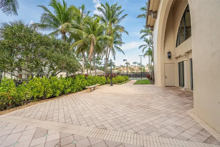 Expansive paver patio with a decorative border, surrounded by lush landscaping and mature palm trees