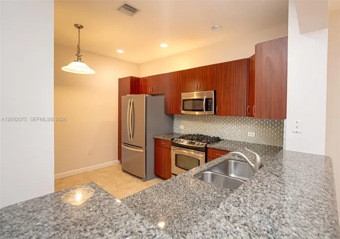Kitchen featuring wood cabinetry, stainless steel appliances, a tile backsplash, granite countertops, and recessed lighting