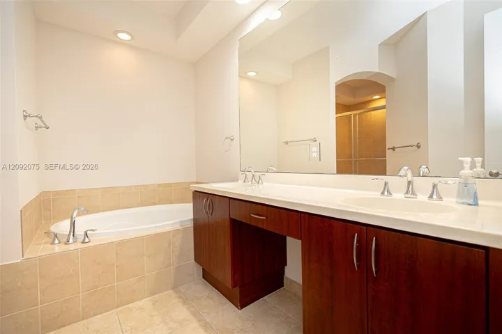Dual vanity with integrated sinks, recessed lighting, built-in soaking tub with tile surround, and wood-finish cabinetry