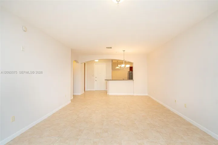 Tile flooring throughout, neutral wall tones, arched doorway, and a kitchen pass-through with a breakfast bar