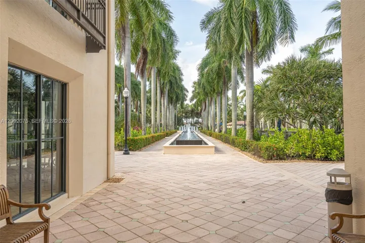 Paved walkway featuring a central water feature, manicured hedges, and mature palm trees