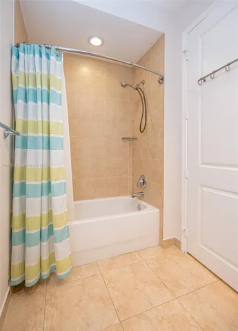 Built-in bathtub with a tile surround, curved shower rod, recessed ceiling lighting, and large format tile flooring