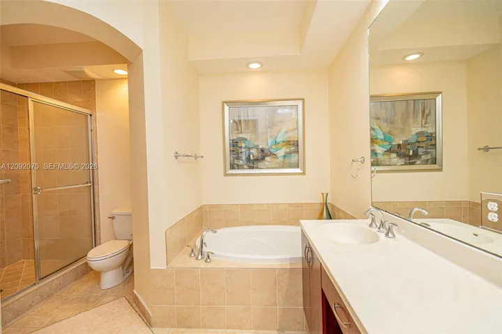 Recessed lighting, arched doorway, fully tiled shower with glass enclosure, soaking tub, and dual vanity with integrated sinks
