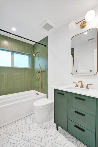 Bathtub with brass-finish fixtures, green subway tile surround, and geometric floor tiling