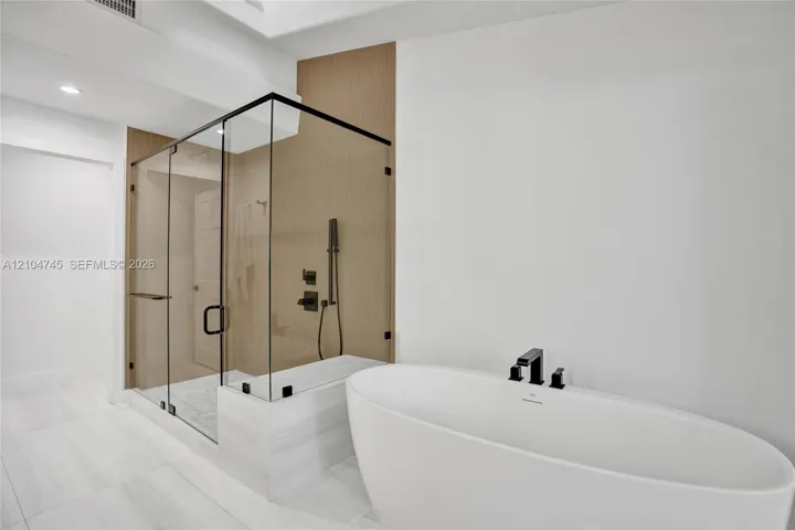 Freestanding soaking tub with matte black fixtures, glass-enclosed shower, shower bench, and light-toned tile flooring