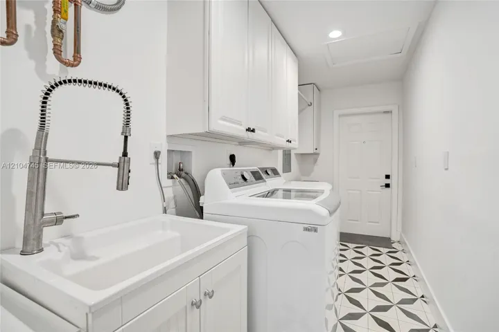 Utility room featuring a built-in sink with a pull-down faucet, upper and lower cabinetry, a patterned tile floor, and a flush-mount ceiling light