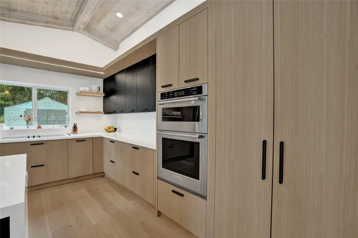 Kitchen featuring a vaulted wood-paneled ceiling, integrated stainless steel appliances, light wood-finish cabinetry, white countertops, and wood-finish flooring