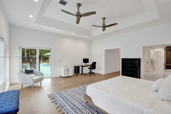 Recessed tray ceiling with integrated lighting, wood-finish flooring, dual ceiling fans, and sliding glass door