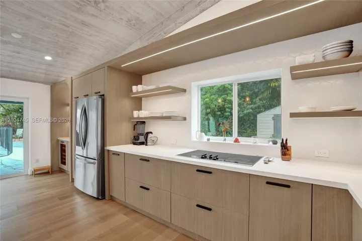 Vaulted wood-finish ceiling, light wood-finish cabinetry, stainless steel appliances, integrated cooktop, and light countertops