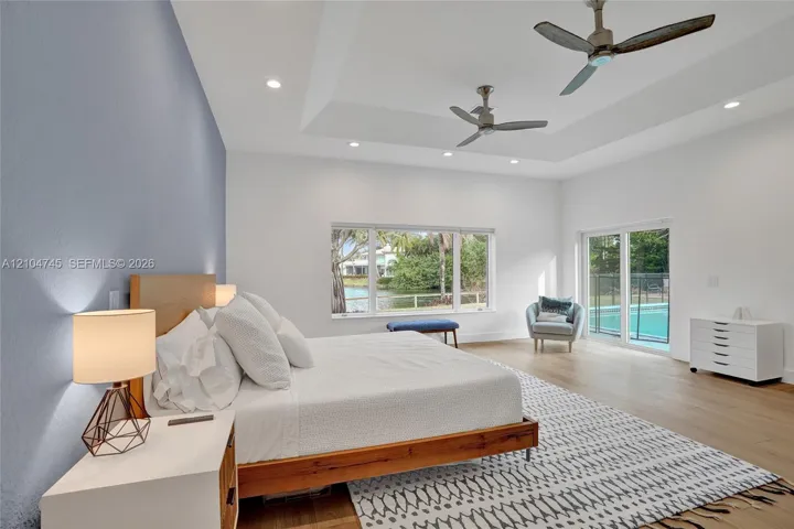 Tray ceiling with recessed lighting and two ceiling fans, wood-finish flooring, and a sliding glass door to the exterior
