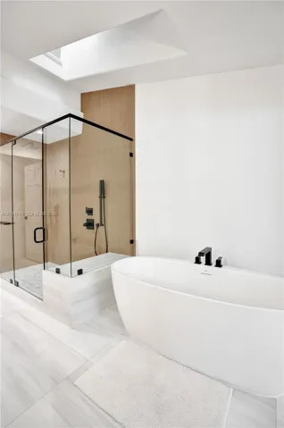 Freestanding soaking tub with matte black fixtures, glass-enclosed shower with matte black shower system, and skylight