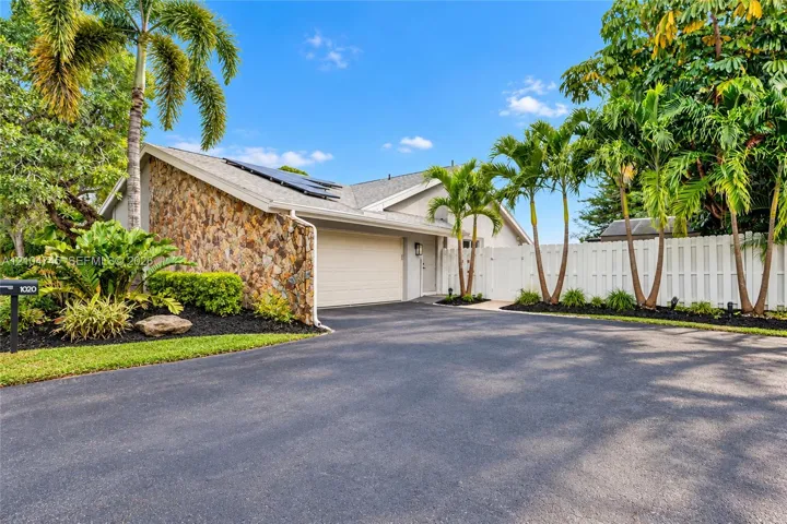 Stone-clad exterior accent, attached garage, well-maintained landscaping, solar panels, and white privacy fencing