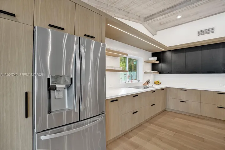 Stainless steel French door refrigerator, light wood-finish cabinetry, dark upper cabinetry, white countertops, and light wood-finish flooring