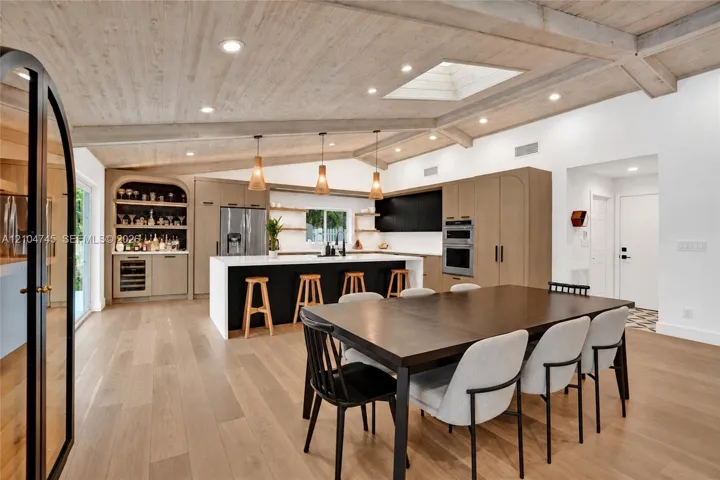 Vaulted wood-finish ceiling with exposed beams, wood-finish flooring, custom built-in bar, center island with stone countertop, and integrated stainless steel appliances