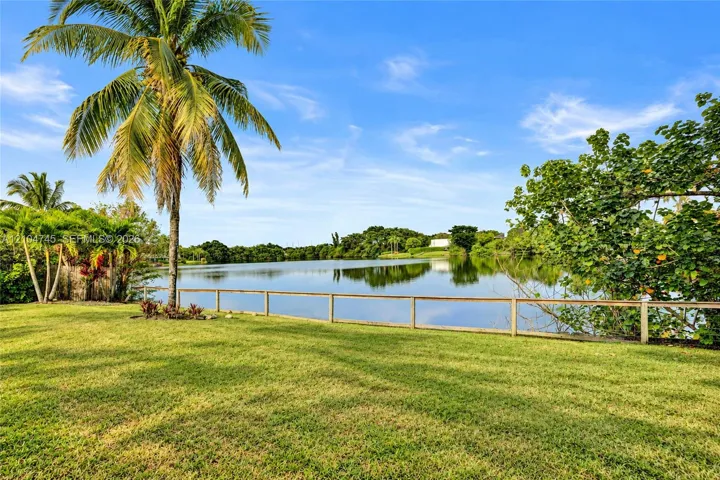 Expansive green lawn with mature palm trees and a wooden fence bordering the tranquil water