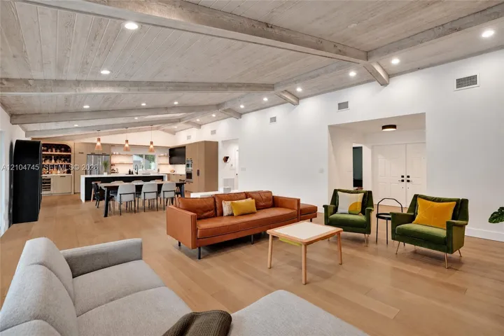 Vaulted ceiling with exposed beams, recessed lighting, wood-finish flooring, built-in kitchen cabinetry, and a large kitchen island with seating