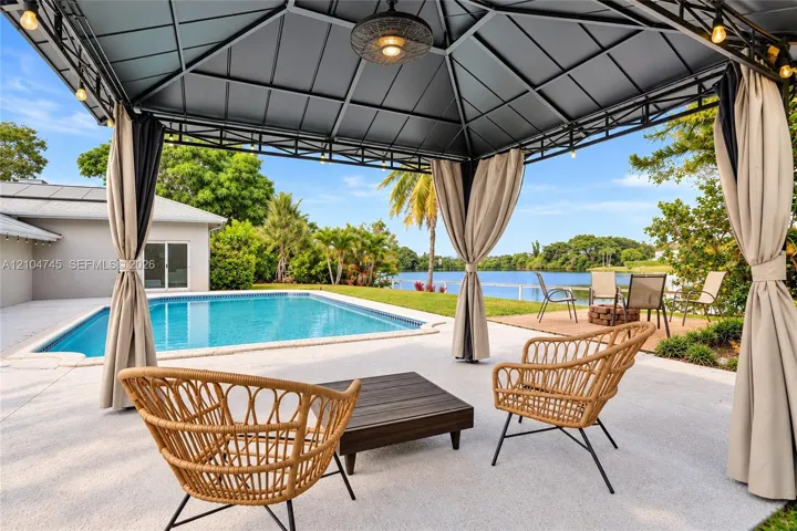 Open-air gazebo with integrated lighting and privacy drapes, expansive patio with a rectangular swimming pool, and solar panels on the roof