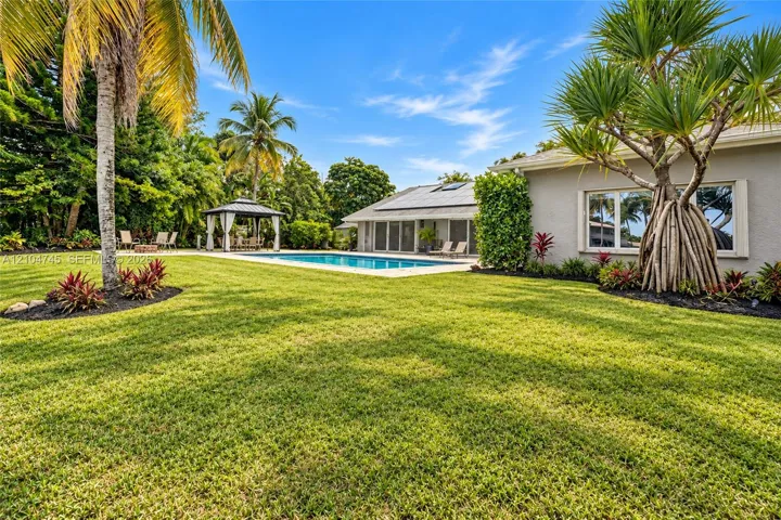 Expansive lawn with mature palm trees, a swimming pool, and a poolside gazebo