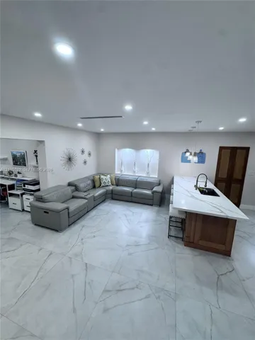 Recessed lighting throughout, large format tile flooring, island with integrated sink, wood-finish cabinetry, and pendant lighting