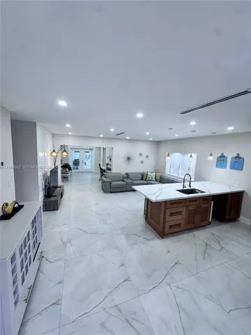 Open-concept living space with large format tile flooring, recessed lighting, and a kitchen island featuring a black sink and faucet