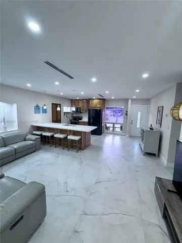 Open-concept living space featuring large format tile flooring, a kitchen island with seating, recessed lighting, and wood cabinetry