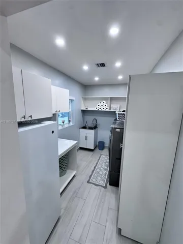 Recessed lighting, wood-finish flooring, built-in shelving, white cabinetry, and a utility sink