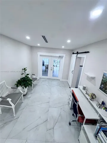 Recessed lighting illuminates the space, featuring large format tile flooring and white french doors