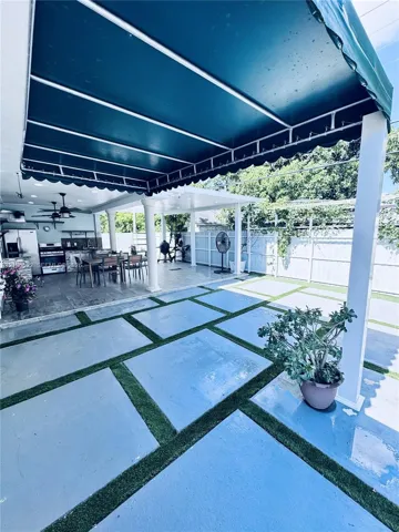 Expansive outdoor space featuring a covered patio, a defined dining area, a large paved patio with artificial turf accents, a built-in outdoor kitchen, and a privacy fence