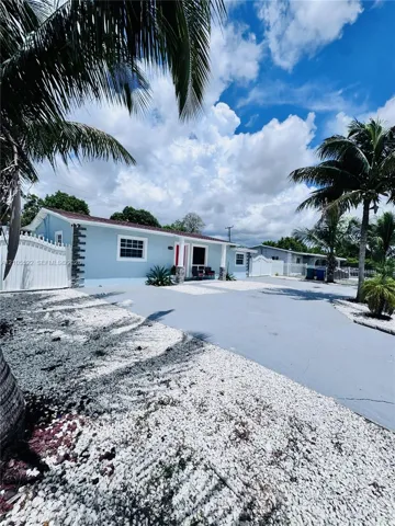 Light blue exterior with white trim, a red entry door, a white privacy fence, an asphalt driveway, and white gravel landscaping