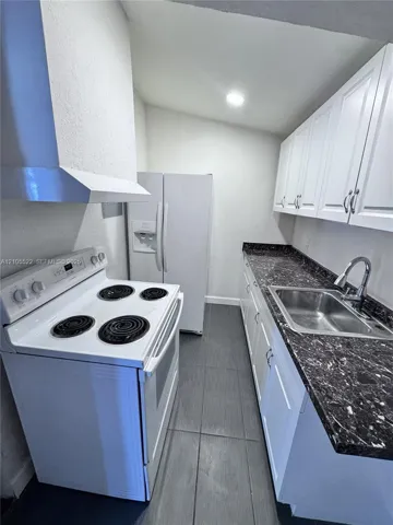 Kitchen featuring white cabinetry, dark countertops, a stainless steel sink with a gooseneck faucet, a white range, and a stainless steel range hood