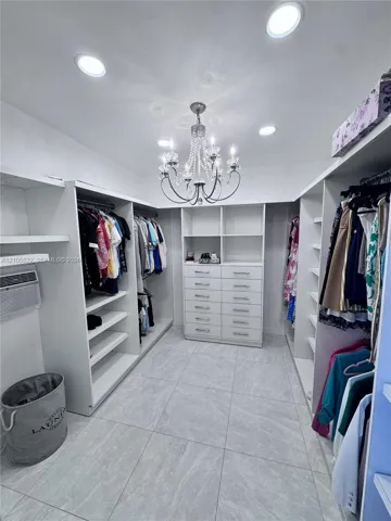 Walk-in closet featuring extensive built-in shelving, integrated drawers, recessed lighting, a central chandelier, and large format floor tiles