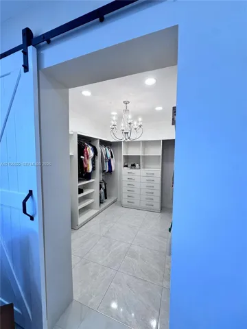 Barn door entry with black hardware, recessed ceiling lighting, crystal chandelier, built-in shelving, and tile flooring